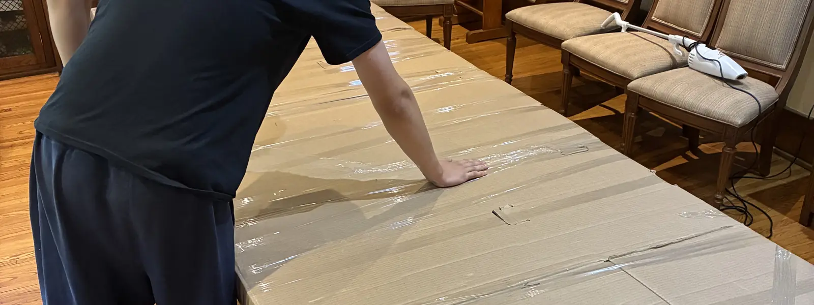 Déménageur qui recouvre une longue table de salle à manger de carton et de pellicule plastique avant le déménagement