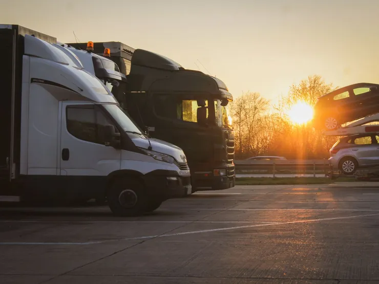 Trucks and a car transporter parked at sunset, cars loaded on the upper deck
