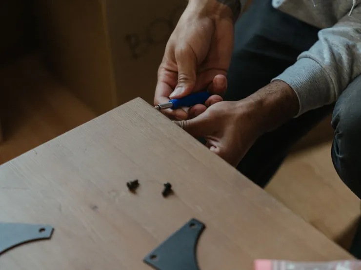 Mains qui assemblent une table en bois au tournevis, quincaillerie disposée à côté