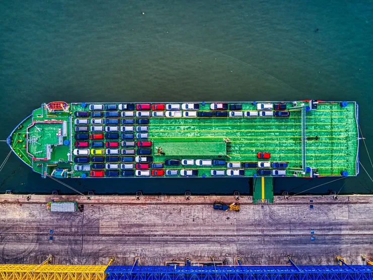 Aerial view of a car-carrying ship at a port with rows of cars on its deck