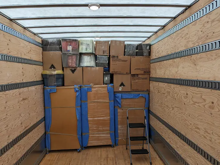 Household boxes and blanket-wrapped furniture loaded and strapped inside a Simplex truck